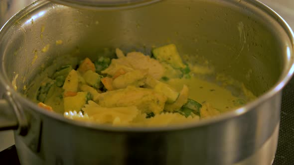 The cook tops boiled pasta in to the steel pot with chicken and green peas, making pasta salad, hand