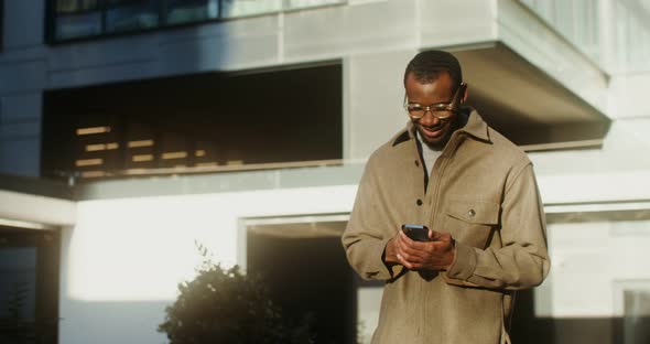 AfricanAmerican Man is Typing on a Mobile Phone While Walking in the City