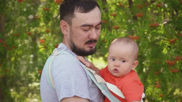 Dad walks with a newborn baby in the park, a child in a sling - a special carrying bag for children