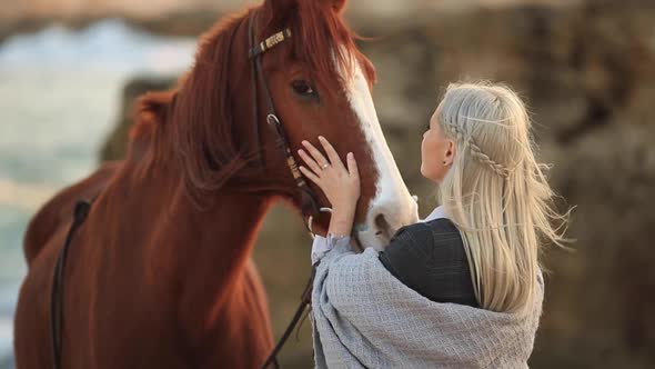 Young Blonde Girl with Long Hair Stroking and Hugging a Horse