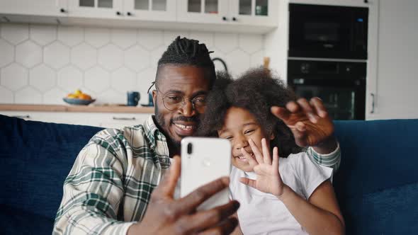 Happy African American Father and Daughter Video Chatting with Relatives Via Smartphone App Sitting