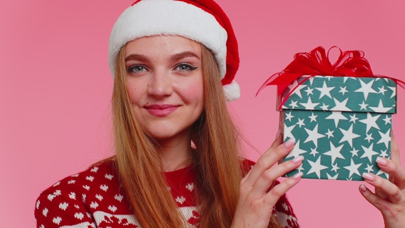 Cheerful Lovely Girl in Sweater Santa Hat Presenting One Christmas Box Excited By Holiday Gift