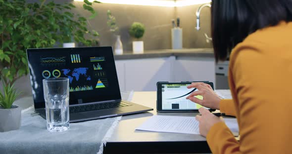 Woman in Stylish Jacket Sitting at Kitchen Table and Working with Documents