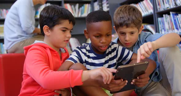 Front view of mixed-race schoolboys studying on digital tablet in the school library 4k