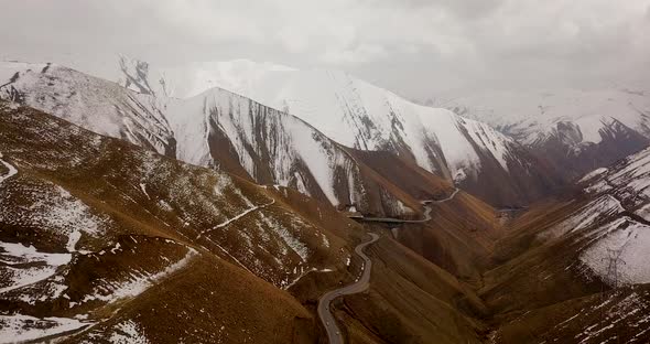 Brown and white mountain with cold frozen ice road and snow covered mountains in clouds and fog in b