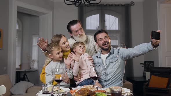 Attractive Happy Family Waving Hands while Making Selfie at the Family Feast