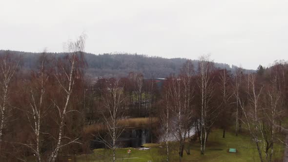 Borås town park with birch trees and river and industrial warehouse in front, aerial ascend shot