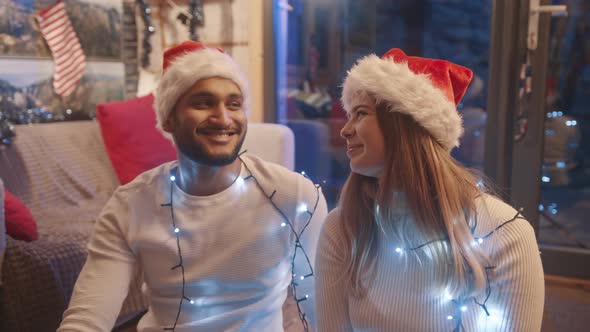 Happy Young Couple with Santa Hats Smiling to Each Other and Flirting