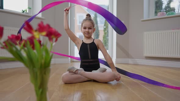 Beautiful Charming Teenage Girl Twirling Gymnastic Ribbon Smiling Sitting on Floor with Bouquet of