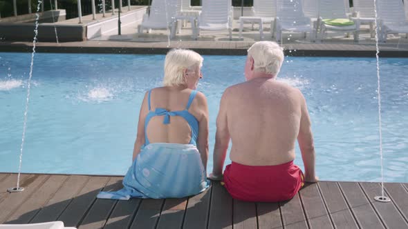 Back View of Happy Mature Couple Sitting on the Edge of the Pool. Cute Senior Man and Woman Relaxing