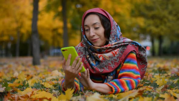 A Beautiful Russian Girl Lies on the Grass in an Autumn Park and Writes a Message on a Light Green