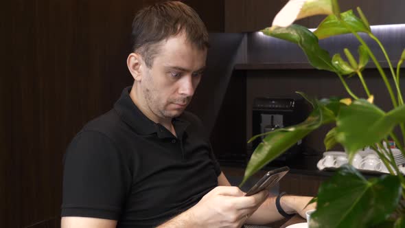 Shocked Man Sitting in Cafe with Cup of Coffee and Reading Bad News on His Phone