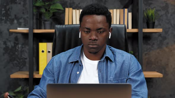 African American Man Works for Laptop in Office Writes Information in Notebook