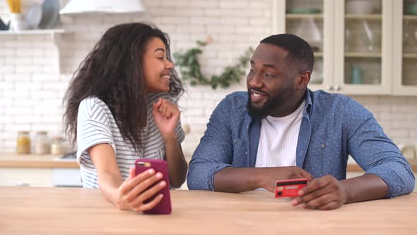 Happy Multiracial Couple Using a Smartphone for Shopping Online at Home