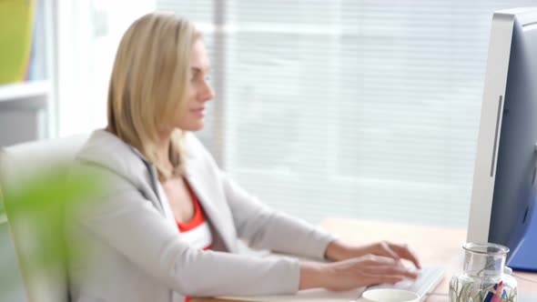 Businesswoman using mobile phone while working on computer