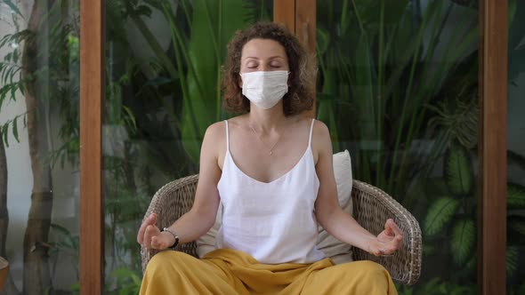 Caucasian Woman with a Protective Face Mask Practicing Yoga in a Space Full of Plants