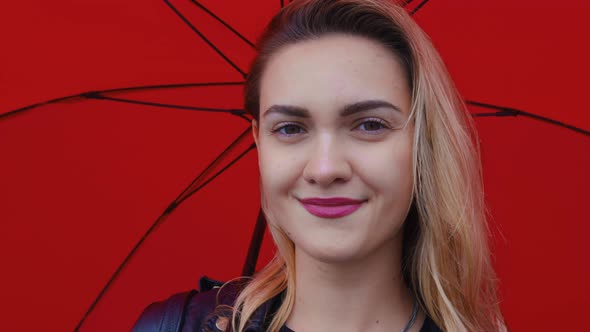 Beautiful Girl Under Red Umbrella Looks at Camera