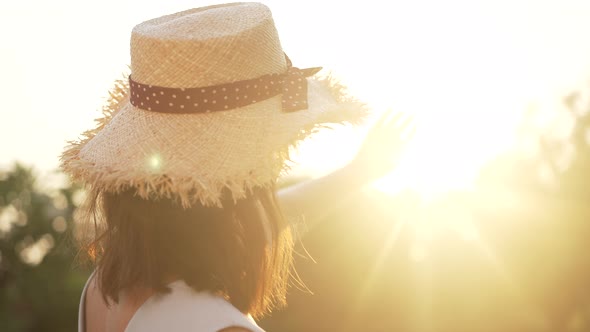 Back View of Charming Caucasian Woman in Straw Hat Stretching Hand to Sunshine Turning to Camera in