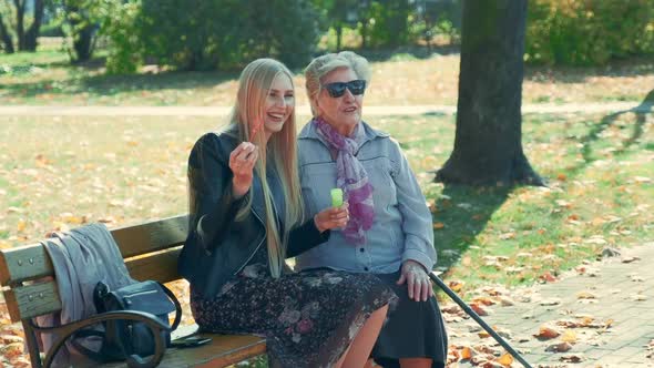 Medium Shot of Happy Young Woman Blowing Bubbles Sitting Together with Her Grandmother in Park