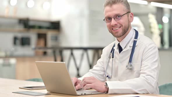 Smiling Male Doctor with Laptop Looking at the Camera 