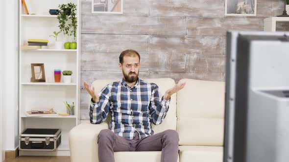 Bearded Young Man Sitting on Couch and Looking Confused at Tv