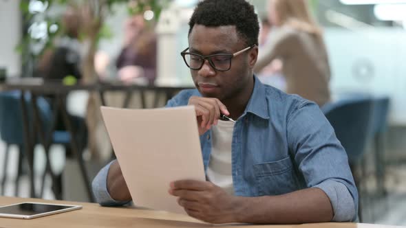 Young African Man Reading Documents in Modern Office