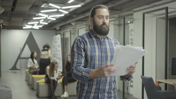 Concentrated Bearded Man Studying Papers Documents Standing in the Office