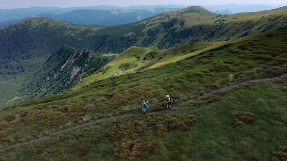 Two hikers with backpacks are walking along mountain range in Carpathian mountains.