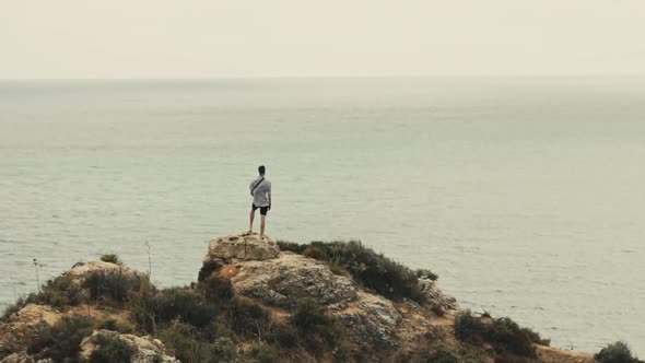 Wide shot showing man standing on rock enjoying beautiful view of Atlantic Ocean. Successful man enj