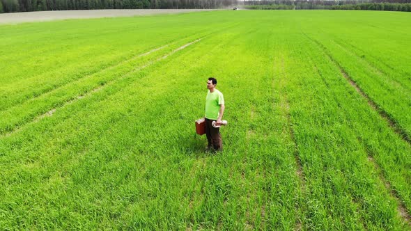 Sad Confused Man Alone Standing in a Green Field, Holding Suitcase in a Hand, Aerial Shot From Drone