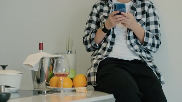 Adult Woman Sit on Kitchen Table and Type Message Text in Smartphone Rbbro