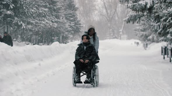 Couple of Asian Guy in the Wheelchair and His Black Girlfriend Walking in Winter Park