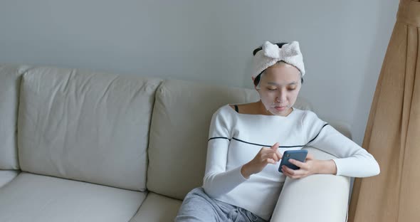 Woman apply paper mask and use of mobile phone at home