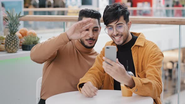 Two Young Arab Guys Friends Looking at Screen Talking on Webcam Using Mobile App on Phone Blogging