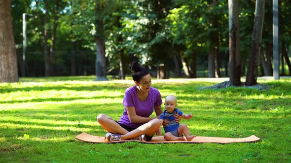 Mother and Baby Sitting on Yoga Mat in Green Park