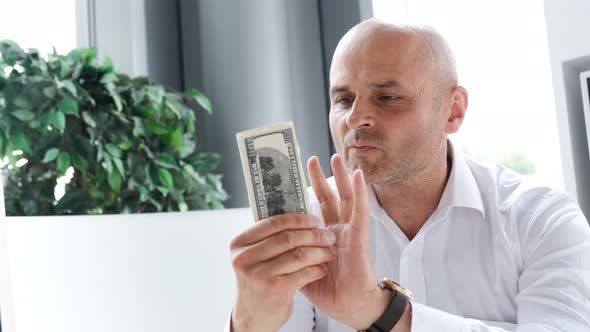 Happy Businessman Counts Dollars While Sitting at a Desk in the Office