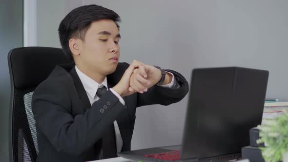 young business man checking time on watch while using laptop