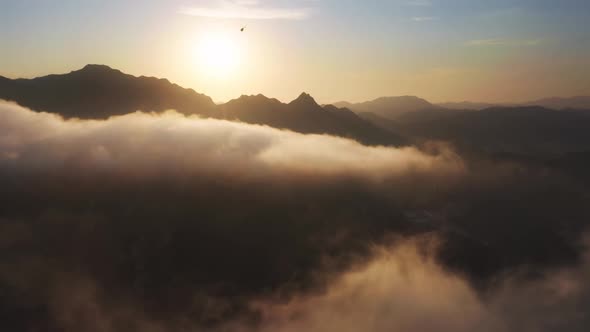 Small Touristic Helicopter Flying Above Clouds and Mountains on Golden Sunset