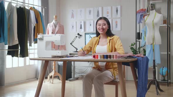 Female Designer With Sewing Machine Smiling To The Camera While Designing Clothes In The Studio