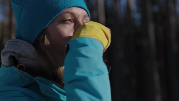 Smiling Blonde Woman Warming Up with Hot Drink in Winter Forest