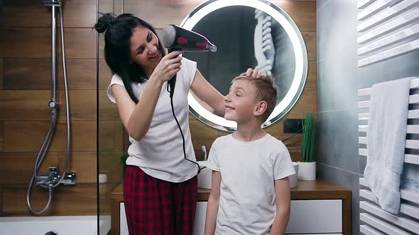 Woman Which Using Hair Dryer Helping to Dry Her Son's Hair in the Bathroom