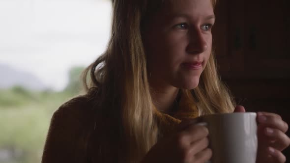 Caucasian woman spending time at home, drinking a beverage, looking at the window