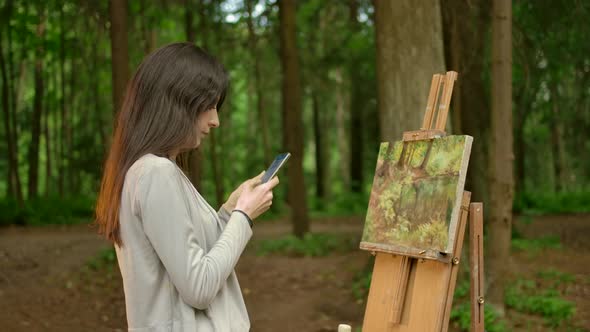 The Girl Artist Completed the Work on Her Painting and Chatting in Her Smartphone