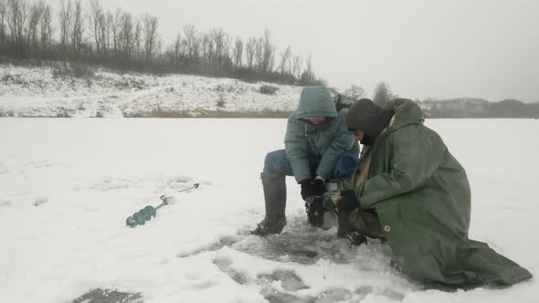 Men are catching fish in ice hole. Winter fishing concept