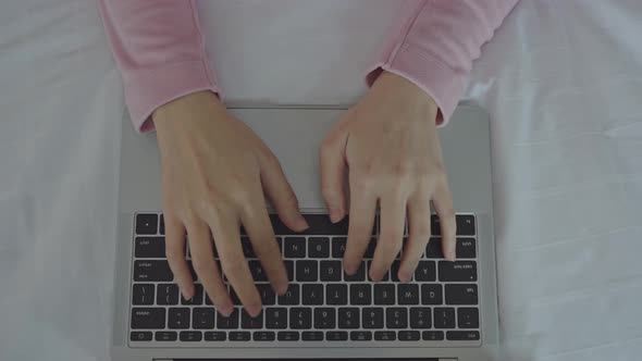 Hands of woman typing on laptop keyboard on bed.