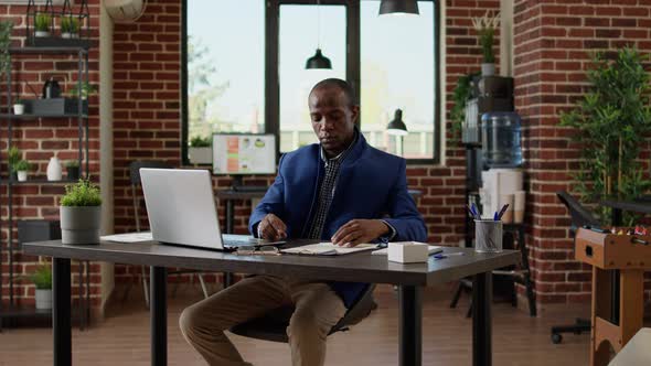 Company Employee Analyzing Project Information on Papers and Laptop