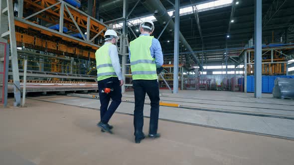 Two Male Engineers Are Walking Along the Industrial Factory Floor