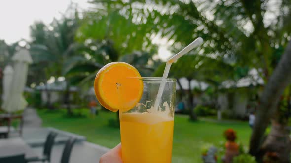Close Up Female Hand Holding Freshly Squeezed Orange Juice with Against the Backdrop of Exotic Green