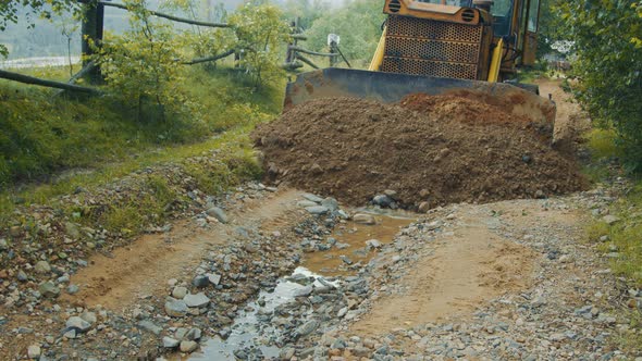 a Bulldozer Levels and Repairs a Road in the Mountains. The Bulldozer Moves Slowly and Covers the