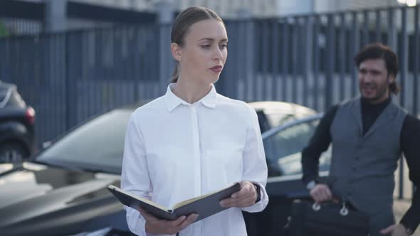 Young Woman Looking Back at Angry Man Talking Gesturing Standing at Car Turning to Camera Sighing